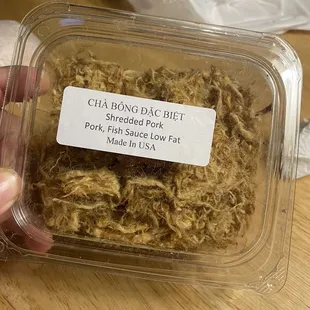 a hand holding a plastic container filled with shredded pork