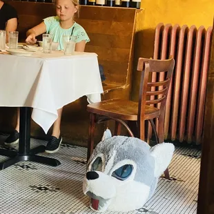 a little girl sitting at a table with a stuffed wolf