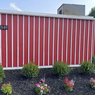 a red and white fence with flowers in front of it