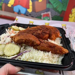 a hand holding a tray of fried chicken and rice