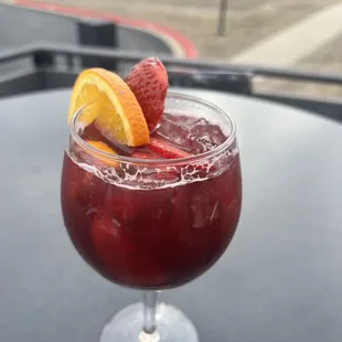 a glass of wine with a garnish of strawberries and oranges