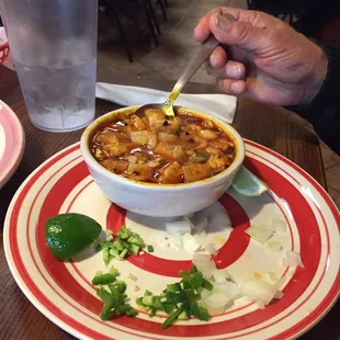A small bowl of Menudo with lime, fresh jalapeños, and chopped onions on the side