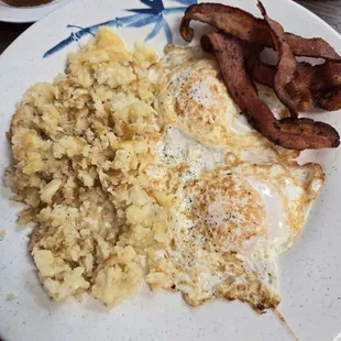 Hash browns, eggs over easy and crisp bacon with white bread toast.