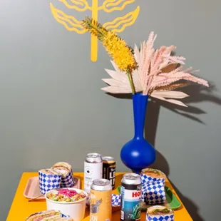 a yellow table with a blue vase and plates of food