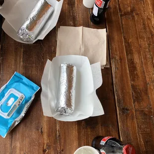 a burrito, a soda, and other condiments on a wooden table