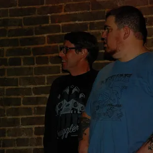 two men standing in front of a brick wall