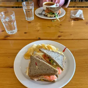 a woman sitting at a table with a sandwich and chips