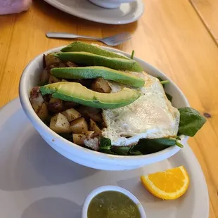 Breakfast bowl - two over-easy eggs, grilled potatoes, fresh avocado slices on a bed of fresh spinach. Side of hot sauce.