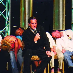 a man in a tuxedo sitting in front of a group of people