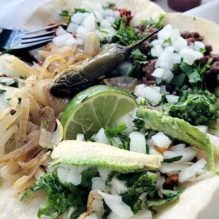 a plate of tacos with onions, avocado, and lime
