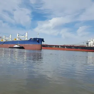 Blue &amp; red ship starting to turn around with help from both tug boats as other passes