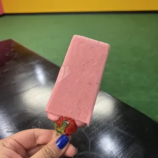 a hand holding a strawberry popsicle