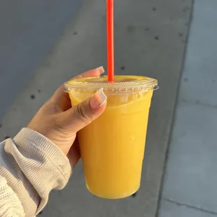 a hand holding a plastic cup of orange juice