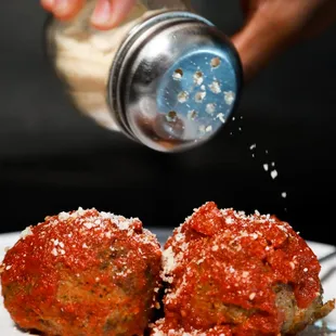 a hand sprinkling salt over a plate of meatballs