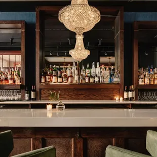 a bar with green chairs and a chandelier
