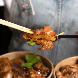 a person holding chopsticks over a bowl of food