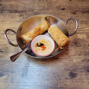 a bowl of dipping sauce and a plate of spring rolls