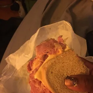 a person holding a sandwich with ham and cheese