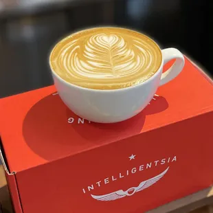 a latte in a white cup on a red box