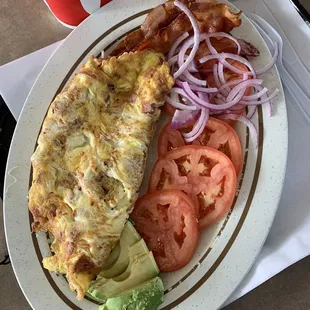Ham and cheese omelette with onions and side of tomatoes slices and side of bacon and avocado and large ice tea