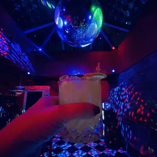 a person holding a drink in front of a disco ball