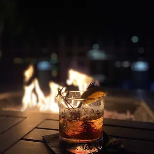 a glass of alcohol on a table with a fire in the background