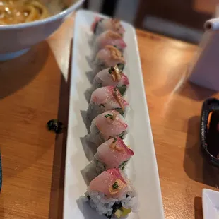 a long plate of sushi with a bowl of soup in the background