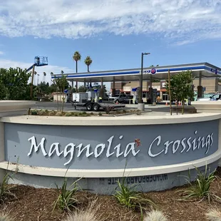 a sign for magnolia crossing in front of a gas station