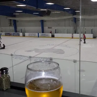 a glass of beer on a table in front of a hockey rink