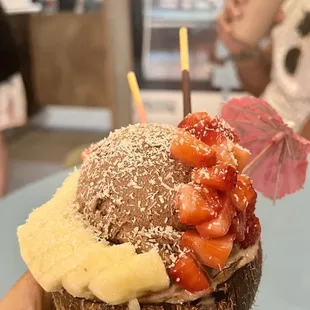 a person holding a coconut shell with strawberries and bananas