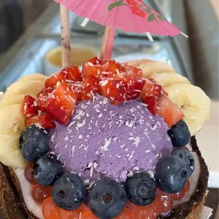 Taro ice cream in coconut bowl with bananas, strawberries, blueberries, popping boba, &amp; coconut flakes