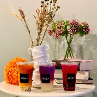 three drinks on a table next to a vase of flowers