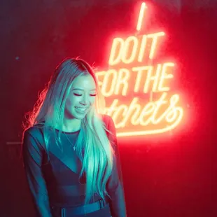 a woman in a black bodysuit and thigh high boots standing in front of a neon sign