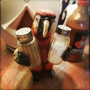 a parrot holding salt and pepper shakers
