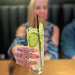 a woman holding a glass with a cucumber in it