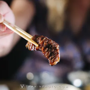 a person holding chopsticks with meat on it