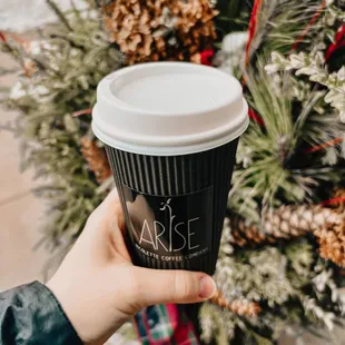 a person holding a coffee cup in front of a christmas tree