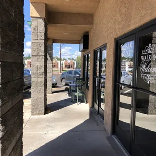 One table and 2 chairs outside coffee shop. Salon next door has two tables with chairs .