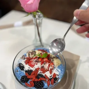 a bowl of fruit and yogurt with a rose in the background