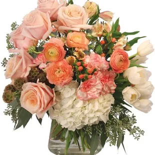 Peach, coral, and white florals with greens in a clear vase.