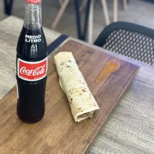 a bottle of coke and a burrito on a table