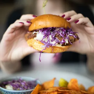 a woman holding a hamburger over a plate of fries