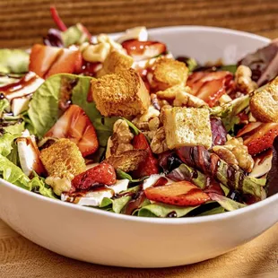 a bowl of salad with strawberries and croutons