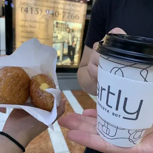 a hand holding a cup of coffee and two doughnuts