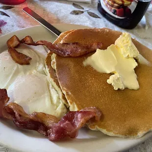 Two large and fluffy pancakes topped with butter. 2 eggs. 2 strips of bacon.