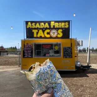 a person holding a burrito in front of a taco truck