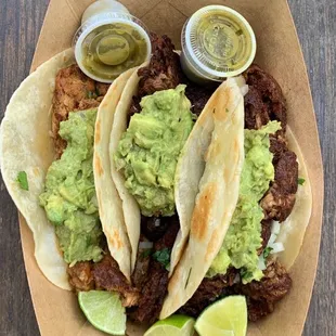 three tacos with guacamole and lime wedges