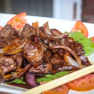 a plate of meat and vegetables with chopsticks