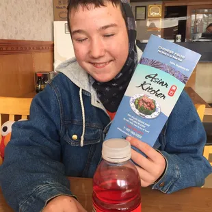 a boy sitting at a table with a bottle of juice