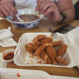 a man sitting at a table with a bowl of soup and a plate of chicken nuggies